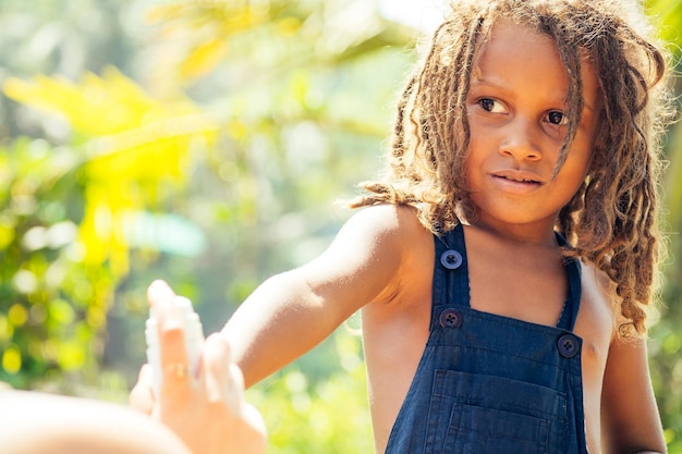 Ragazzo indiano Mowgli con i capelli dreadlocks che si nascondono tenendo lo spray per zanzare in uno sfondo di foresta verde tropicale