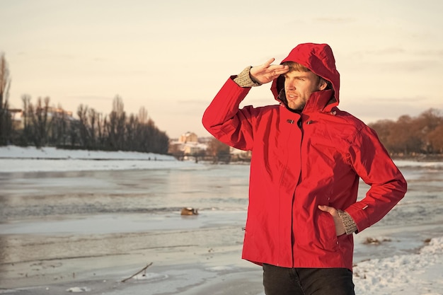 Ragazzo indossa giacca con cappuccio in una gelida giornata invernale Uomo barbuto stand giacca calda sfondo natura innevata Abbigliamento resistente al vento Abbigliamento uomo invernale Abbigliamento per passeggiate invernali Abito invernale hipster caldo