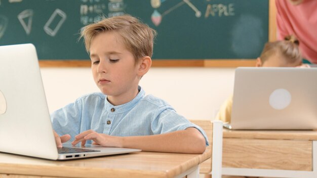Ragazzo intelligente che lavora al portatile mentre diversi bambini programmano la pedagogia del sistema