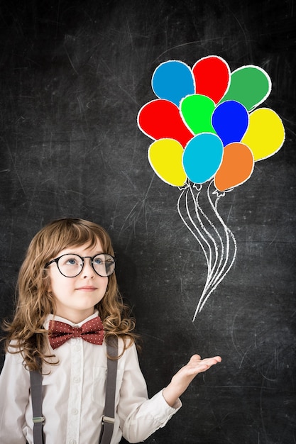 Ragazzo intelligente in classe. Bambino felice contro la lavagna con disegno di palloncini colorati. Concetto di educazione