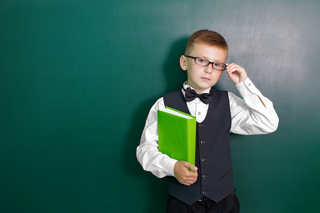 Ragazzo intelligente sveglio felice con un farfallino e in vetri con il libro in sua mano.