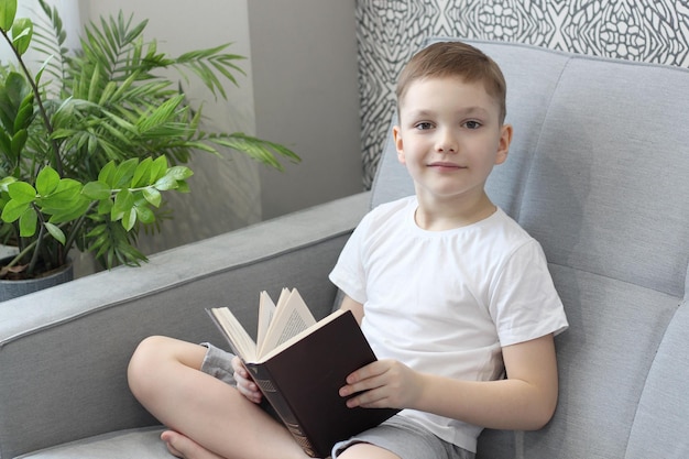 ragazzo legge un libro sul divano di casa. foto chiara nei toni del grigio bianco