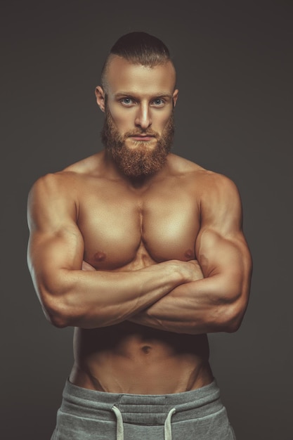 Ragazzo muscoloso della barba con le braccia incrociate isolato su sfondo grigio.