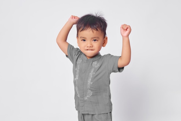 Ragazzo musulmano asiatico bambino eccitato in piedi con vittoria celebrazione isolato su sfondo bianco studio