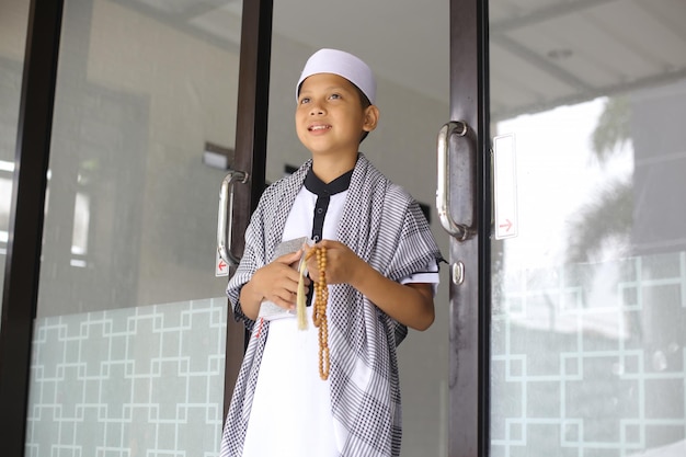 Ragazzo musulmano sorridente che tiene al quran e tasbih ed esce dalla moschea