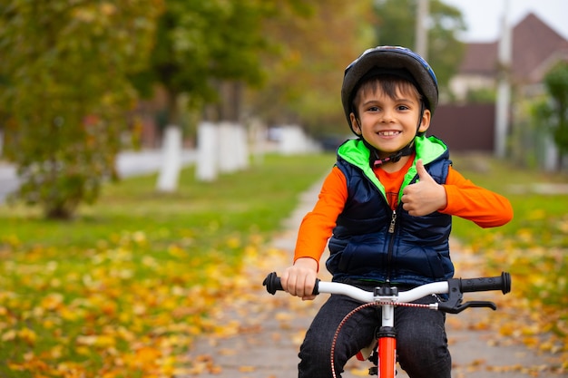 Ragazzo nel parco d'autunno in bicicletta. Un bambino piccolo mostra la classe. Sport all'aria aperta sani e attivi. Foto con spazio vuoto.