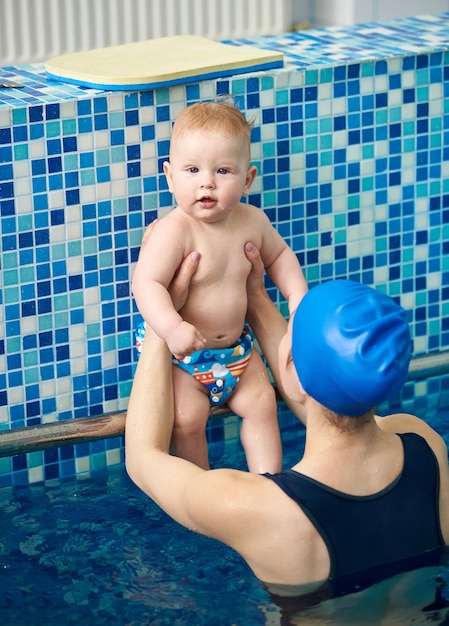 Ragazzo neonato che guarda nella fotocamera tempo attivo che riposa con la madre nella piscina per bambini Mamma che prepara il futuro nuotatore