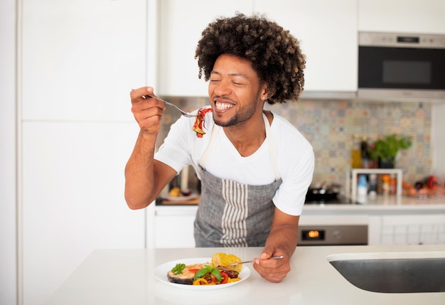 Ragazzo nero allegro che mangia la sua cena fatta in casa nella cucina moderna