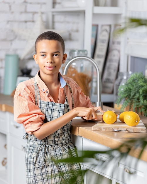 Ragazzo nero ragazzo che cucina limone fresco in cucina a casa bambino africano che si prepara sul tavolo