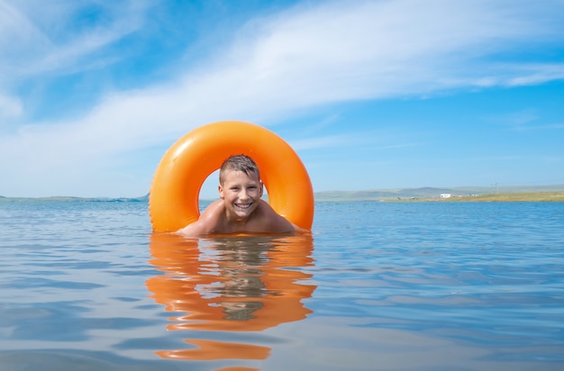ragazzo nuota nel lago in una giornata di sole estivo galleggia con un anello galleggiante arancione e sorride