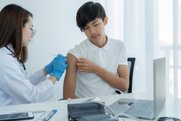 Ragazzo paziente con il medico che tiene in mano una siringa e stava per vaccinare un paziente in clinica per prevenire la diffusione del virus.