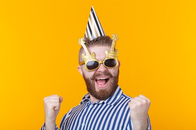 Ragazzo pazzo giovane hipster positivo con la barba ride allegramente su un muro giallo