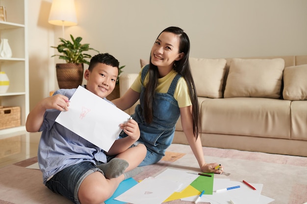 Ragazzo preteen sorridente fiero che mostra l'immagine che ha disegnato con sua madre