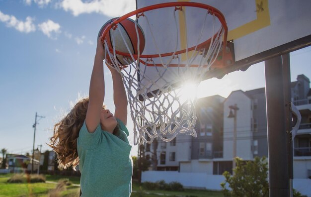 Ragazzo ragazzo giocatore di basket con una palla segnando un obiettivo Giocatore bambino segnando slam dunk stock photo all'aperto nel parco giochi