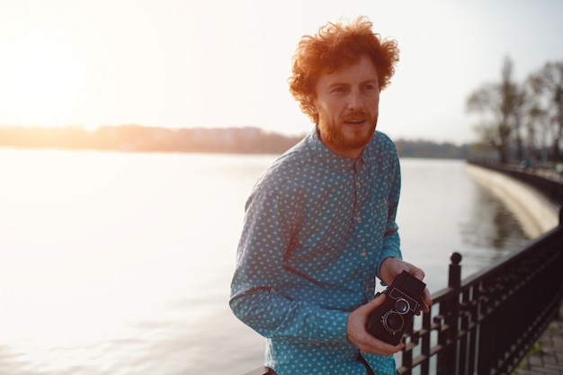 Ragazzo riccio con una macchina da presa di medio formato nelle sue mani vicino al lago