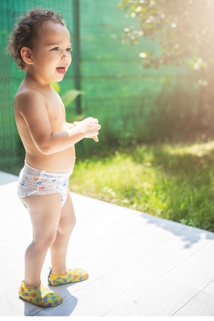 Ragazzo riccio felice del bambino in un pannolino che gioca nel cortile al sole