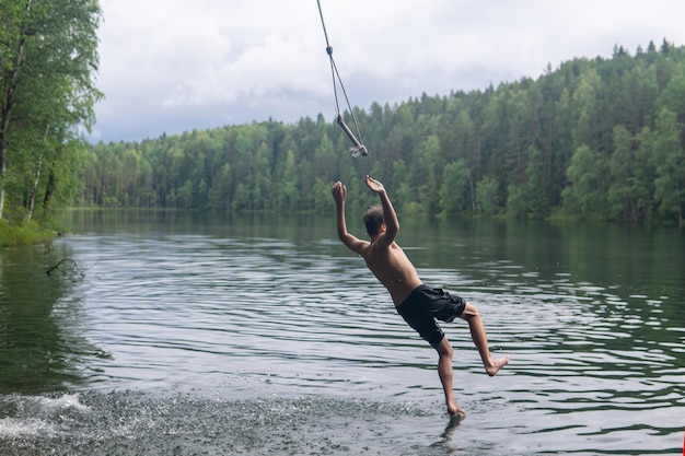 ragazzo salta in acqua usando un'altalena tarzan mentre nuota in un lago forestale