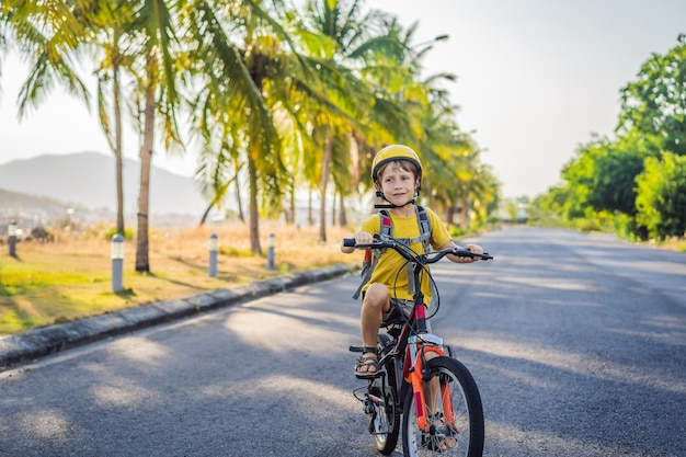 Ragazzo scolastico attivo con casco di sicurezza che va in bicicletta con lo zaino in una giornata di sole Bambino felice in bici sulla strada per la scuola Cammino sicuro per i bambini all'aperto per la scuola