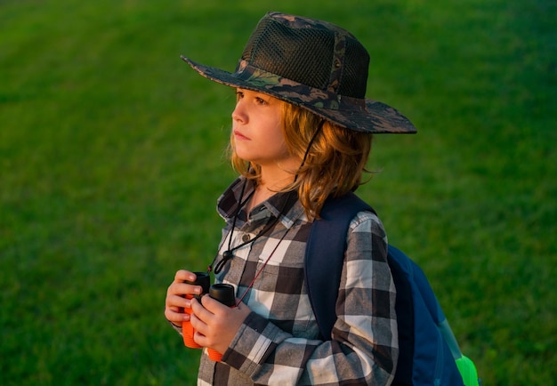 Ragazzo scout che indossa cappello da esploratore e zaino all'aperto Esploratore e avventura con il binocolo