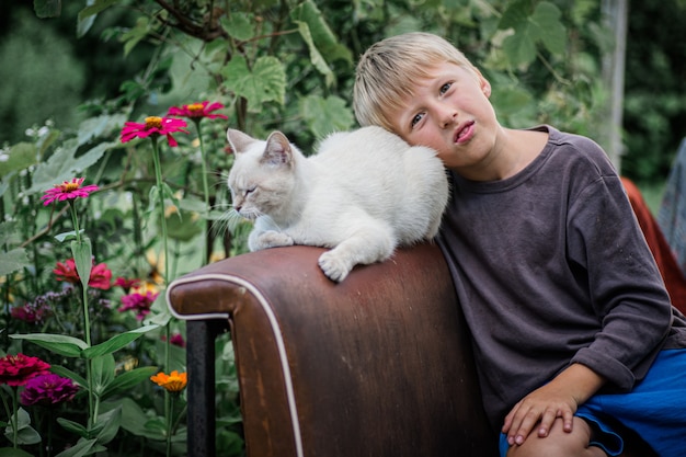 Ragazzo seduto accanto al gatto. Prendersi cura di animali domestici. gatto bianco all'aperto tra i fiori.