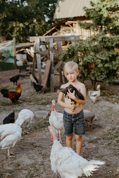 Ragazzo senza camicia che tiene la gallina in piedi al pollame