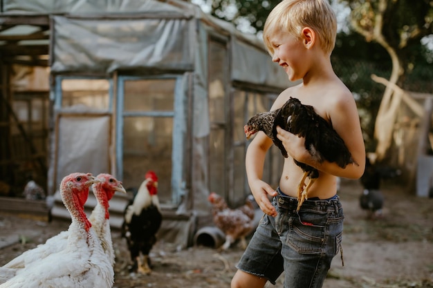 Ragazzo senza camicia che tiene un pollo in piedi all'aperto