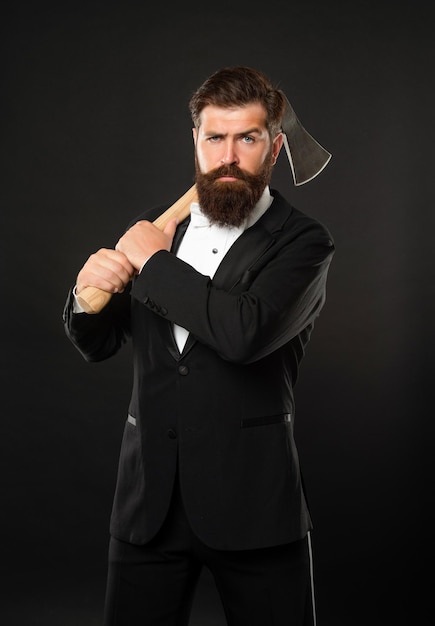Ragazzo serio con la barba lunga con barba e baffi in abito formale che tiene ascia sfondo scuro uomo barbuto