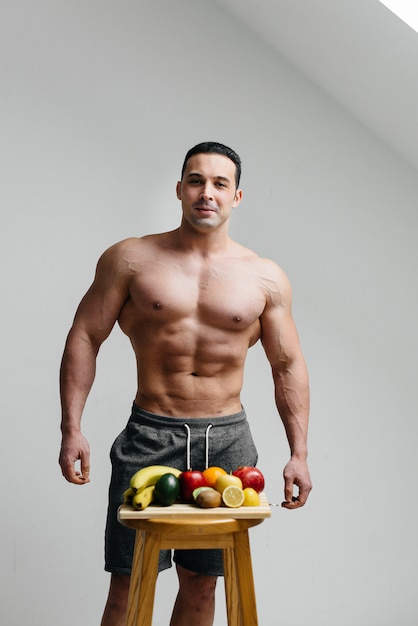 Ragazzo sexy vegano con un torso nudo in posa accanto alla frutta. Dieta. Dieta sana.