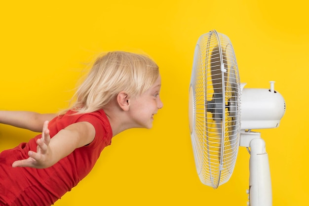 Ragazzo si raffredda con il ventilatore Ritratto su sfondo giallo Calore estivo