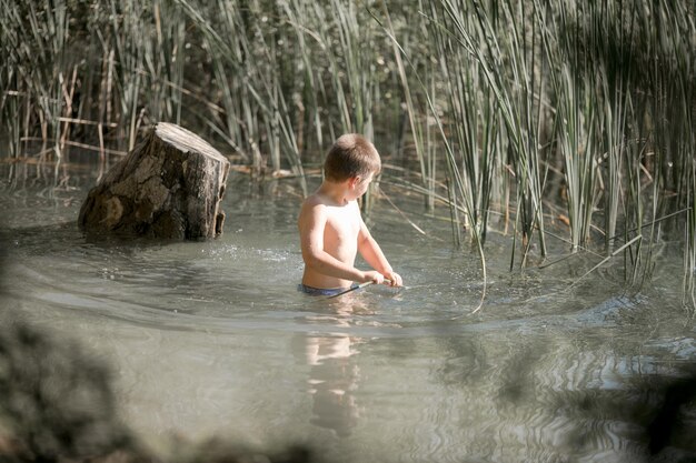 Ragazzo solitario ammirando la bellezza del lago d'estate in Grecia Ragazzo che gioca fuori imita la pesca in un lago