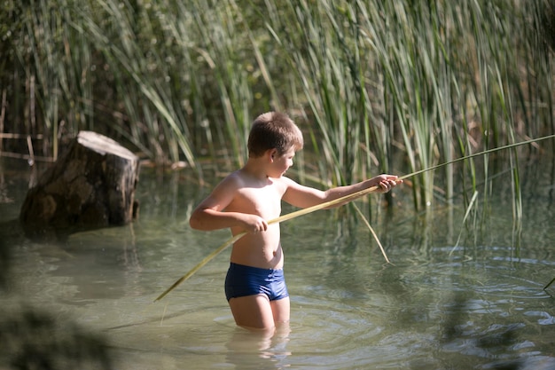 Ragazzo solitario ammirando la bellezza del lago d'estate in Grecia Ragazzo che gioca fuori imita la pesca in un lago