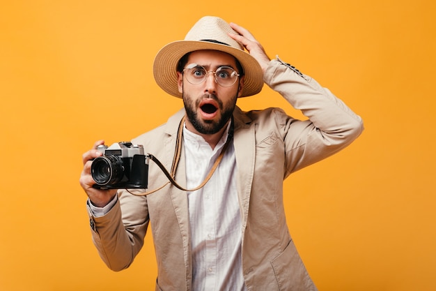 Ragazzo sorpreso in cappello e vestito beige che tiene macchina fotografica retrò