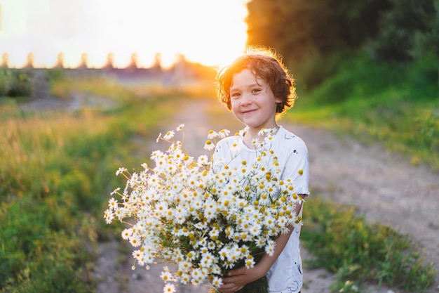 Ragazzo sorridente carino al campo di camomilla al tramonto in una luce solare morbida La vita senza allergie respira liberamente Ragazzo e margherite Bambino che sogna e sorride sullo sfondo di un campo di camomilla