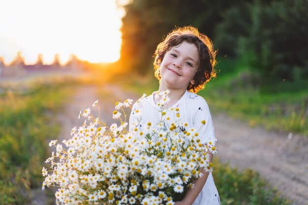 Ragazzo sorridente carino al campo di camomilla al tramonto in una luce solare morbida La vita senza allergie respira liberamente Ragazzo e margherite Bambino che sogna e sorride sullo sfondo di un campo di camomilla