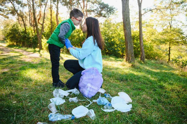 Ragazzo sorridente che raccoglie spazzatura nel parco con sua madre. Concetto di volontariato.