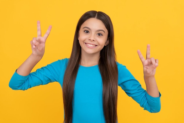 Ragazzo sorridente con capelli lunghi bellezza e moda femminile modella aspetto grazioso di giovane ragazza viso ritratto di bambino su sfondo giallo esprimere emozioni positive gesto di pace