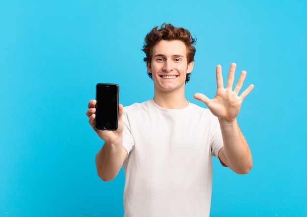 Ragazzo sorridente e dall'aspetto amichevole, mostrando il numero cinque o il quinto con la mano in avanti, conto alla rovescia. concetto di schermo del telefono