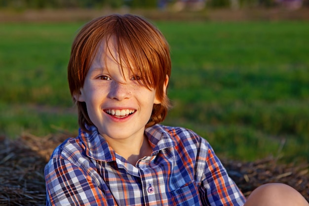 Ragazzo sorridente felice con i capelli rossi e le lentiggini nel ritratto del campo di circa 8 anni di estate