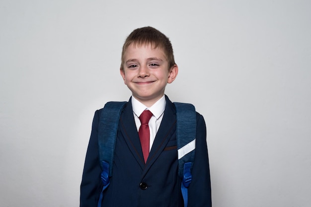 Ragazzo sorridente in uniforme scolastica e zaino su sfondo bianco Ritratto a mezza lunghezza del concetto di scuola media superiore