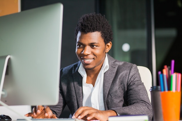 Ragazzo sorridente laborioso in ufficio guarda il monitor del computer