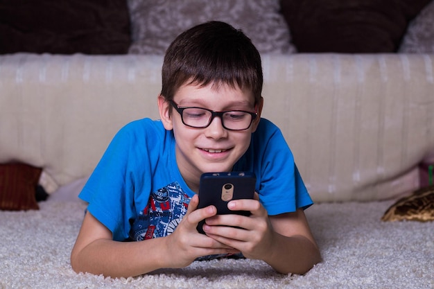 Ragazzo sorridente sdraiato sul pavimento di fronte alla telecamera e guardando lo smartphone