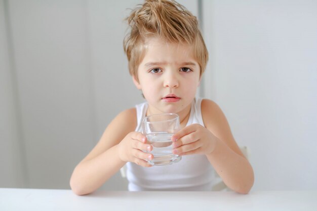 Ragazzo sorridente sveglio con bicchiere d'acqua isolato su un fondo bianco