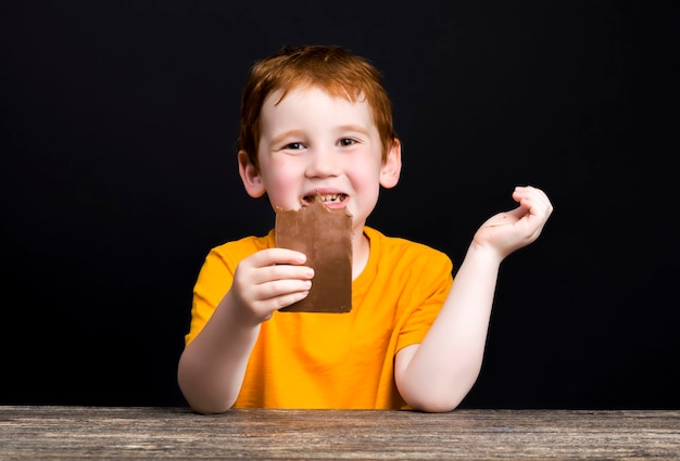 Ragazzo spalmato di cioccolato al latte dopo aver rosicchiato e morso il vero cioccolato al cacao in una barra closeup ritratto di un bambino