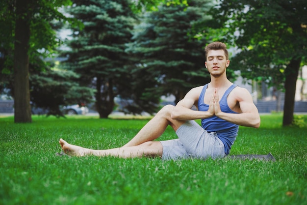 Ragazzo sportivo che pratica yoga seduto sull'erba nel parco. Giovane che medita con gli occhi chiusi, namaste sull'erba verde nel parco, copia spazio