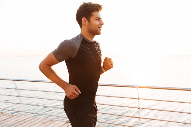 Ragazzo sportivo in tuta da jogging lungo il molo o il lungomare in riva al mare, durante l'alba