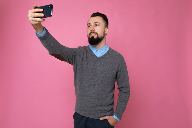 Foto ragazzo su uno sfondo rosa prende un selfie