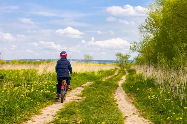 Ragazzo sulla bici sulla strada campestre nel giorno soleggiato