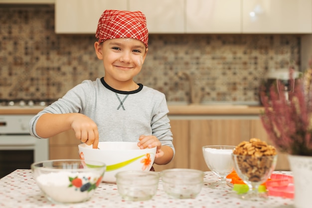 Ragazzo sveglio che cucina nella cucina a casa che guarda alla macchina fotografica