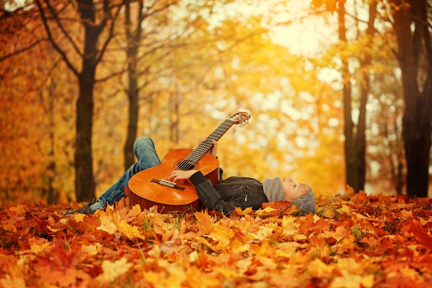 Ragazzo sveglio con la chitarra, trovantesi sull'erba nel giorno soleggiato di autunno