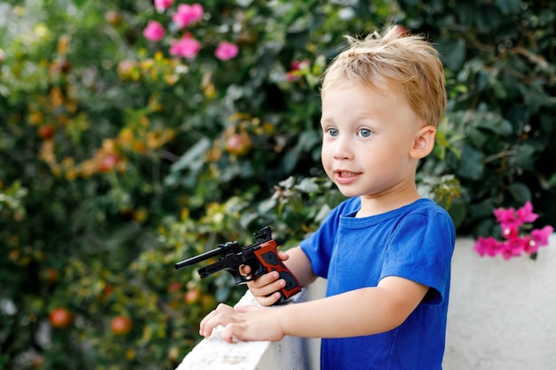 Ragazzo sveglio del bambino con la pistola del giocattolo in giardino